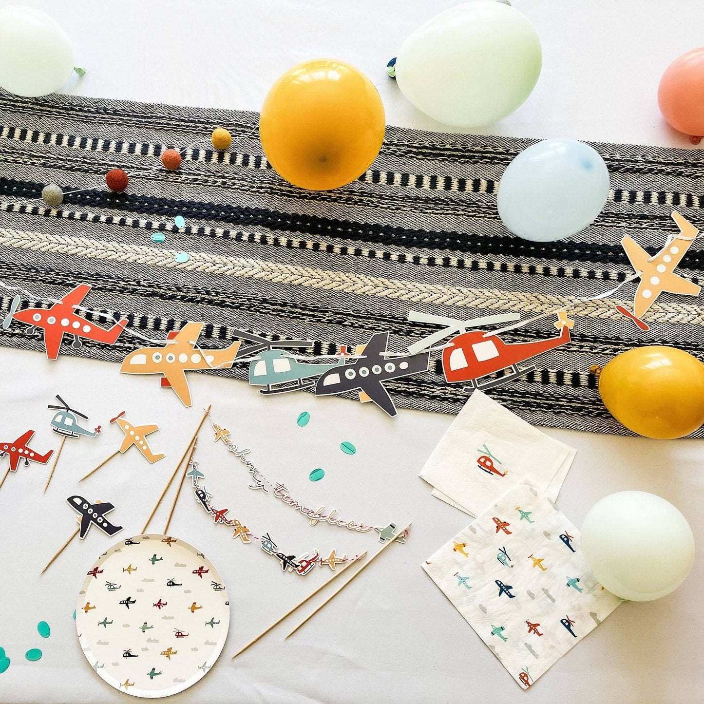 Colorful airplane-themed party supplies including straws, napkins, and balloons on a white surface.
