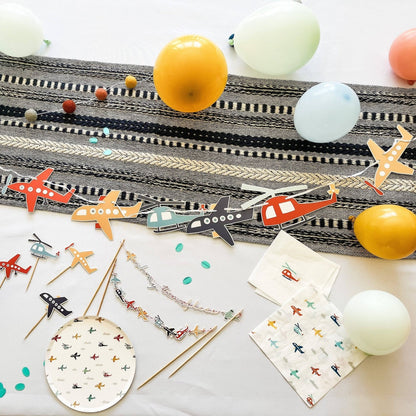 Colorful airplane-themed party supplies including straws, napkins, and balloons on a white surface.