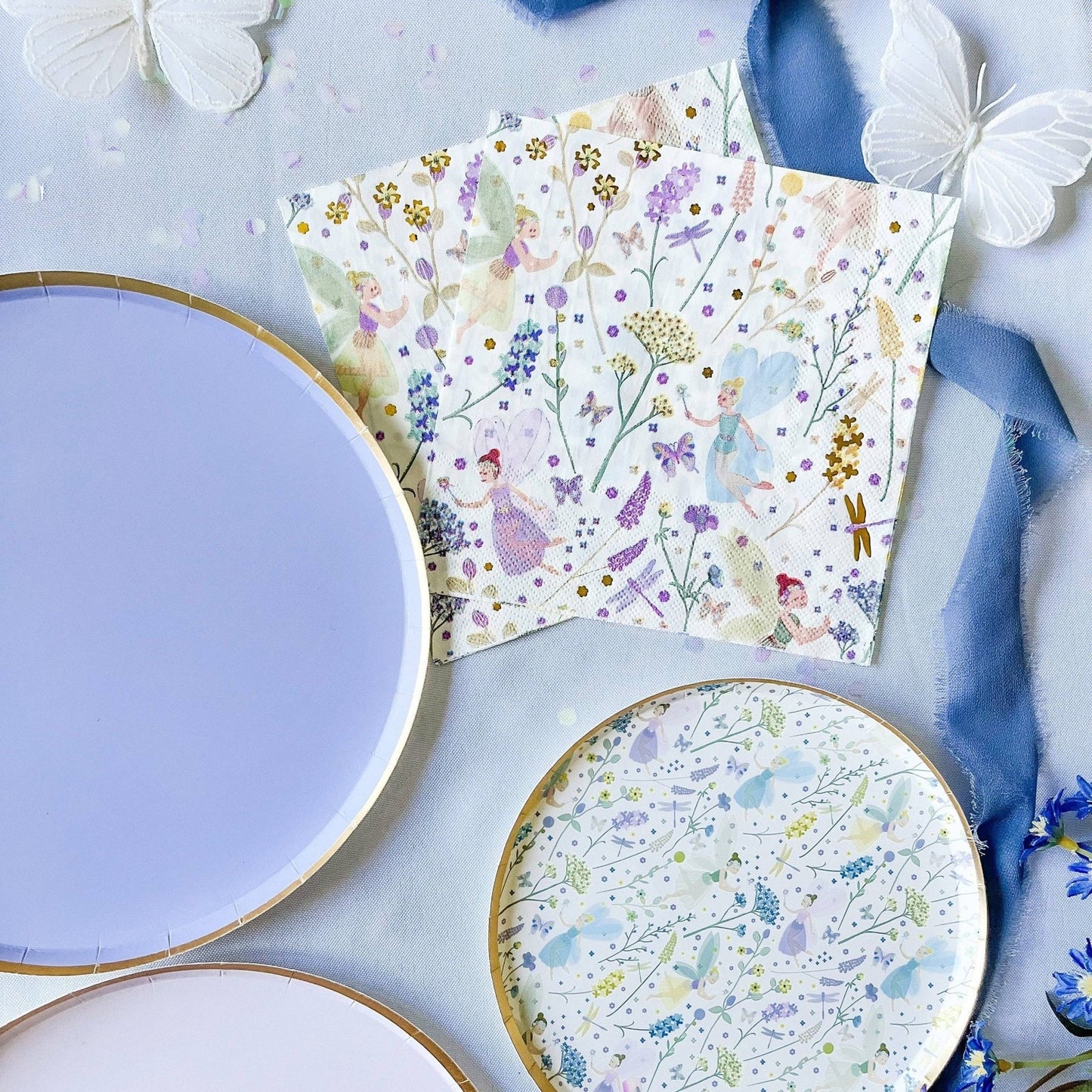 Floral-patterned paper plates and napkins on a light blue surface with decorative elements.