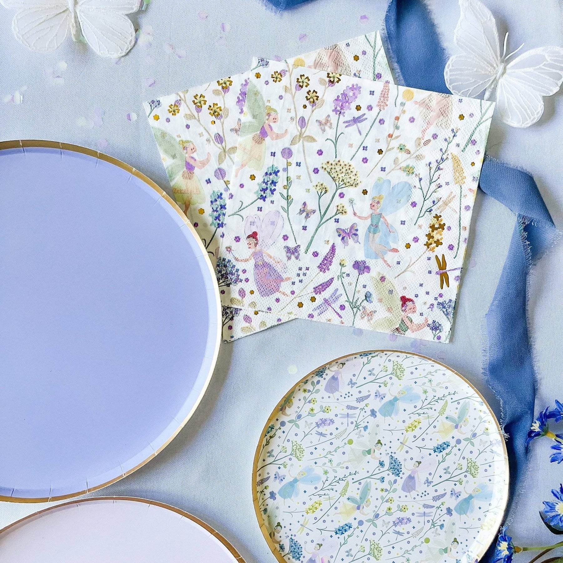 Floral-patterned paper plates and napkins on a light blue surface with decorative elements.