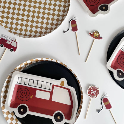 Fire truck-themed paper plates and cupcake toppers on a white surface with checkered placemats.