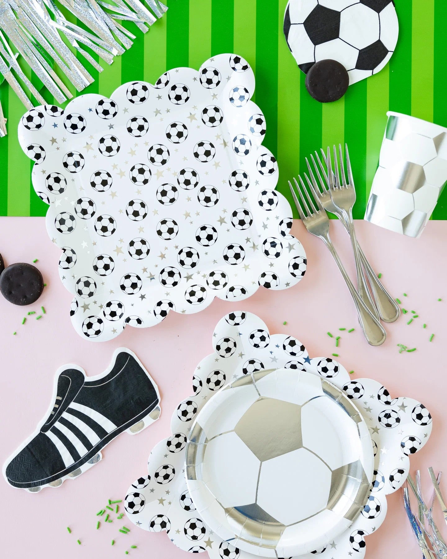 Soccer-themed party supplies including plates, cutlery, and a shoe napkin on a green striped background.