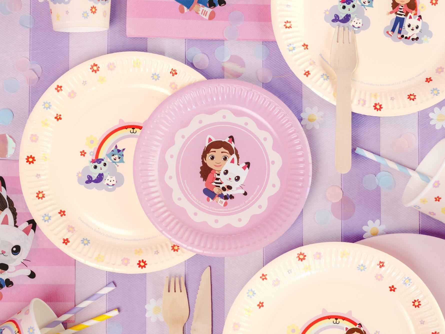 Gabby Dollhouse party tableware with plates, cups, and cutlery on a purple tablecloth.