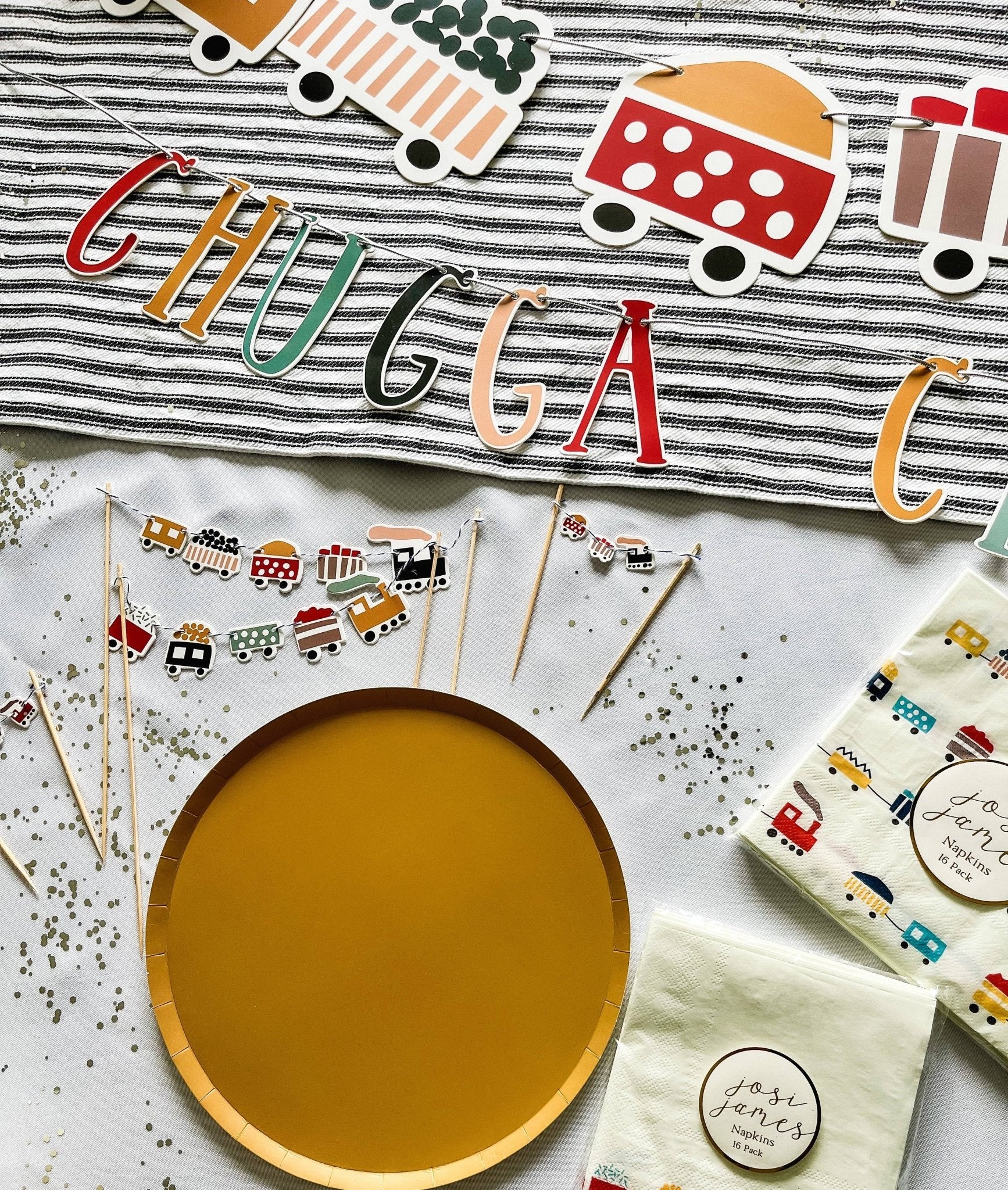 Party supplies with 'CHUGGA CHUGGA' banner, wooden plate, and decorative items on a white surface.