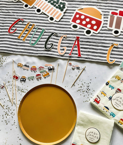 Party supplies with 'CHUGGA CHUGGA' banner, wooden plate, and decorative items on a white surface.