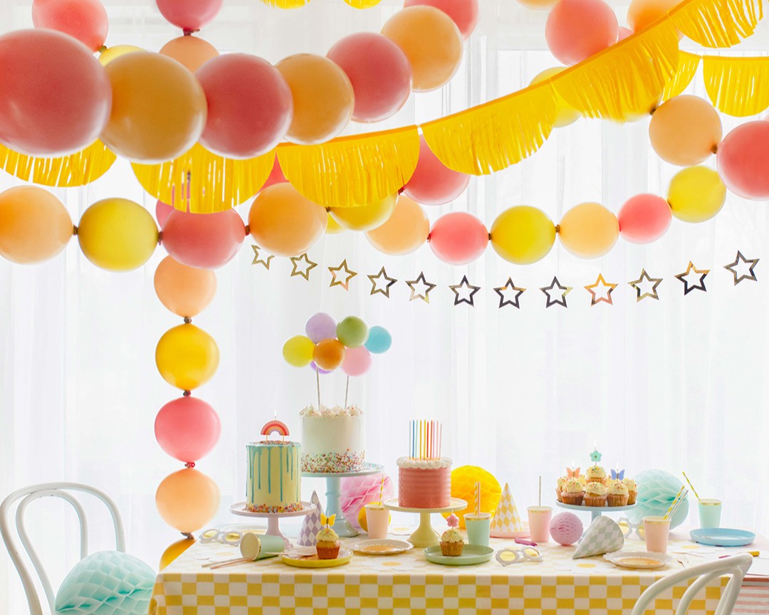 Colorful balloon arch and table setup with cake and decorations in a room.