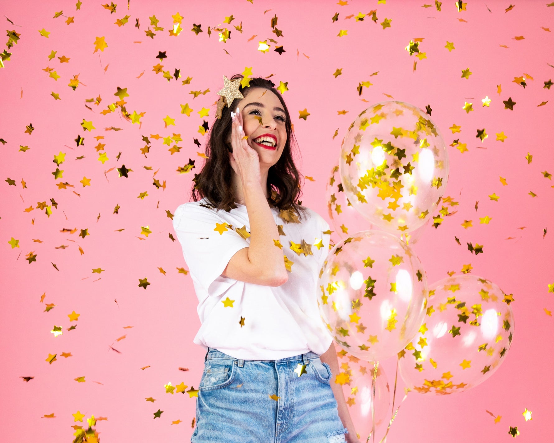 Woman with gold confetti and balloons on a pink background