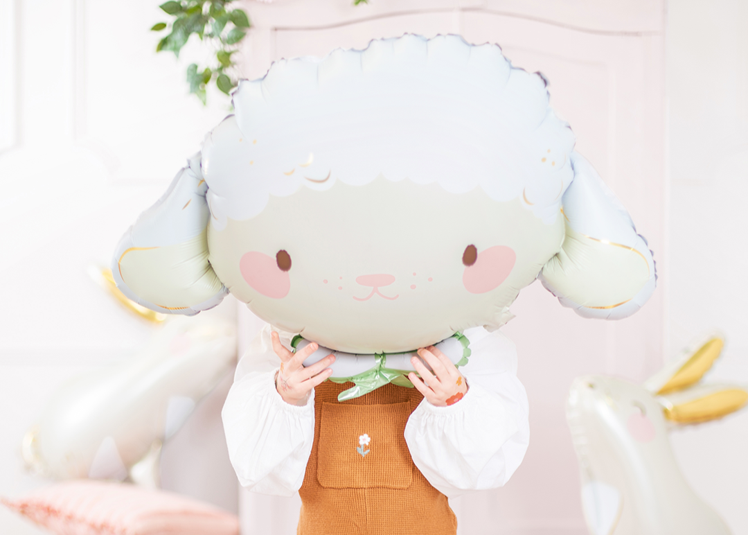 Kid holding a large, sheep foil balloon with a floral background