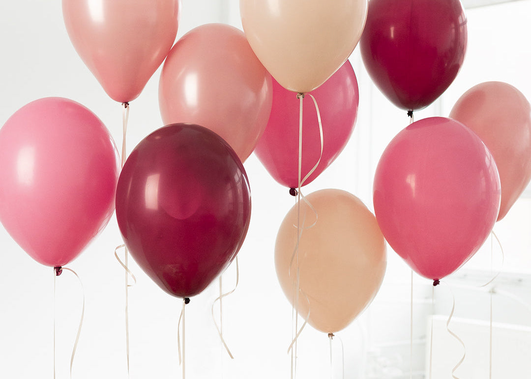 Group of pink, red, and beige balloons against a white background