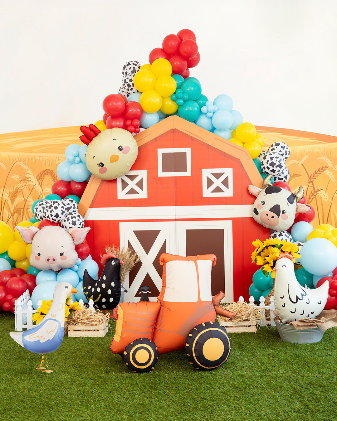 Colorful barn-themed inflatable set with animals and balloons on a grassy background