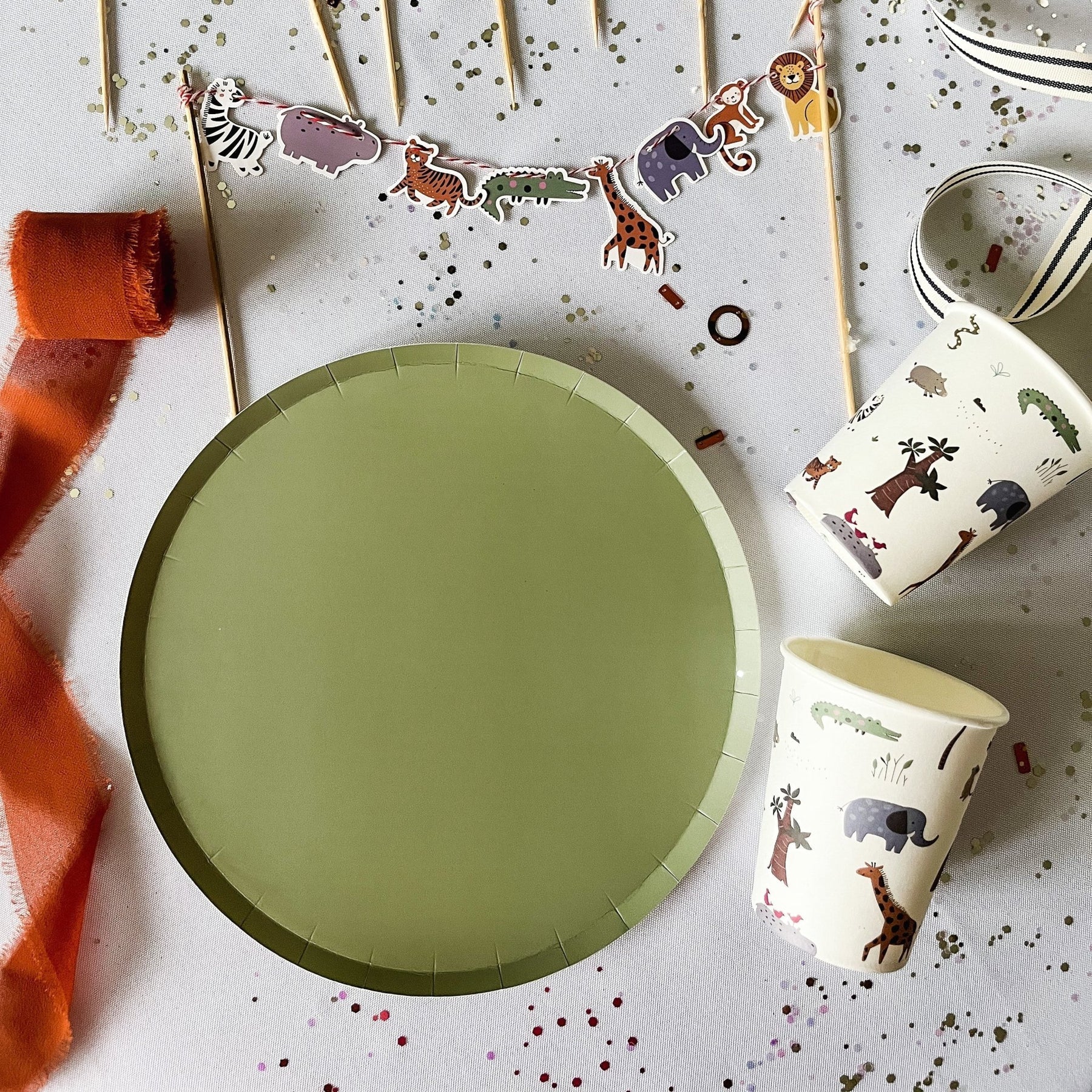 Green paper plate with animal-themed cups and decorations on a light background